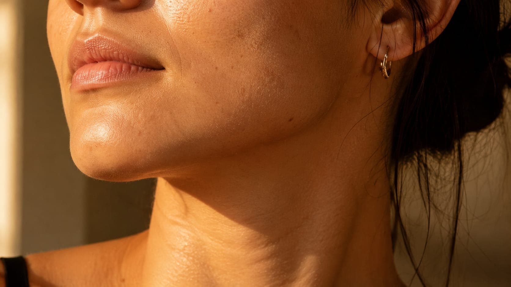 Close-up of a woman's jawline and chin in warm amber light, showing natural skin texture — the jawline is the primary site of androgen-driven acne in PMOS
