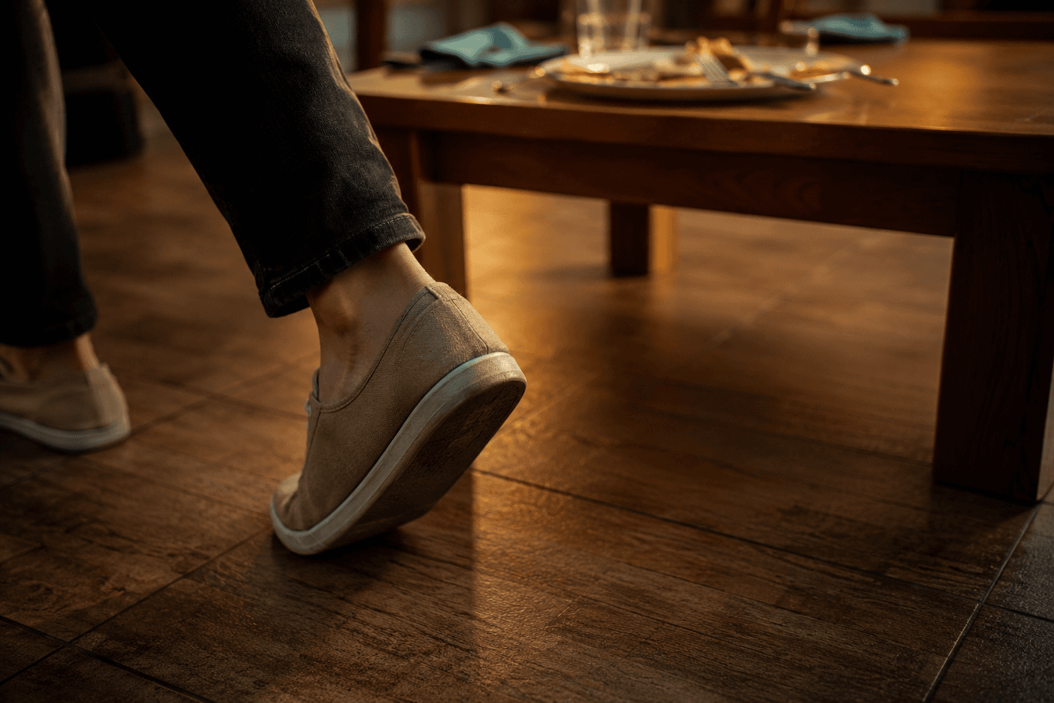 Close-up of feet in casual shoes walking away from a dining table with a blurred plate visible in the background